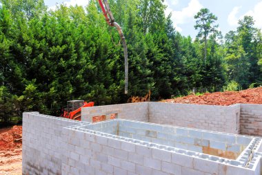 İşçiler verimli yeşillikler arasında inşa edilmiş temel duvarlara beton döküyorlar..