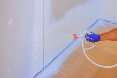 Boyacı odadaki duvarları boyamak için sprey tabanca kullanıyor, iş günü evdeki gelişmeleri gösteriyor..