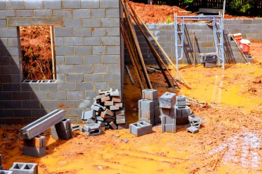 İnşaat çalışmalarının devam ettiği istiflenmiş bloklar, araçlar, inşaat alanındaki çamurlu zemin.