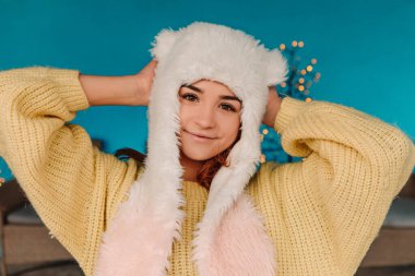 Sıcak süveter ve yün şapka giyip poz vererek kutlama yapan genç ve güzel bir kadın. Kış tatili panayırı, seyahat ruhları beldesi. Yılbaşı süsleri, çelenkler