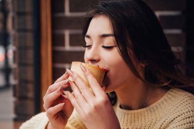 Sıcak kazak giymiş gülümseyen bir kadın, tatlı yemekten hoşlanan, lezzetli bir kek. Sokak kafesinde abur cubur. Yılbaşı süsleri, çelenkler