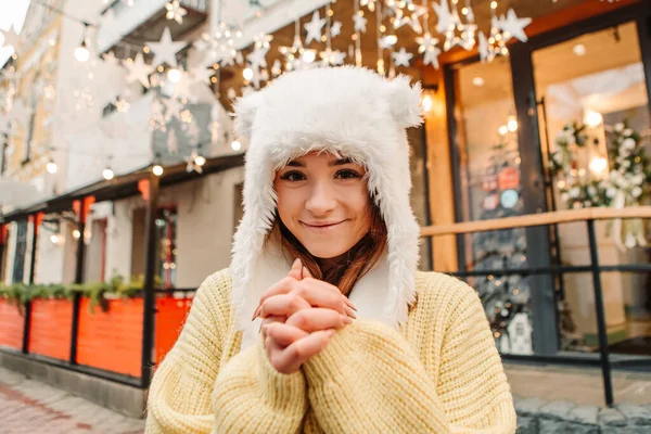 暖かいセーターとウールの帽子を身に着けていることを祝う笑顔の女性は 外にポーズ 冬の市場の休日フェア 旅行精神リゾート 新年のクリスマスの装飾 ガーランド — ストック写真