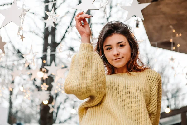外でポーズをとる暖かいセーターを着た笑顔の女性 冬の市場の休日フェア 旅行精神リゾート 新年のクリスマスの装飾 ガーランド — ストック写真
