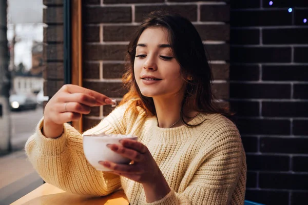 stock image Smiling woman dressed warm sweater, drink marshmallow with milk coffee cacao or latte. Hot aromatic chocolate beverage. Warming snack food in street cafe. New Year Christmas decorations, garlands