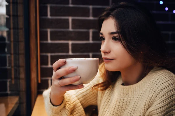 stock image Smiling woman dressed warm sweater, drink marshmallow with milk coffee cacao or latte. Hot aromatic chocolate beverage. Warming snack food in street cafe. New Year Christmas decorations, garlands