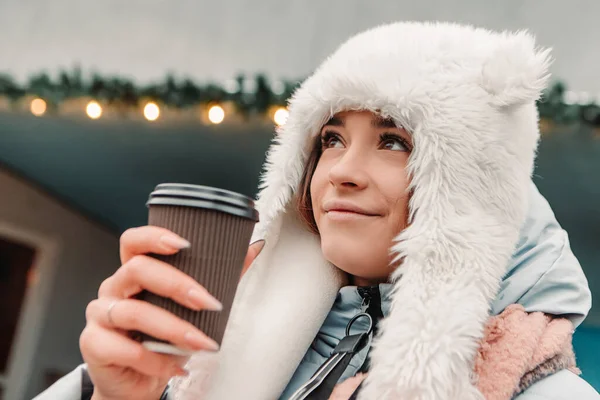 暖かいジャケットとウールの帽子を身に着けていることを祝う若いかなり笑顔の女性は ホットティーコーヒー飲料マルチワインを飲みます 冬の休日 旅行精神リゾート 新年のクリスマスの装飾 ガーランド — ストック写真