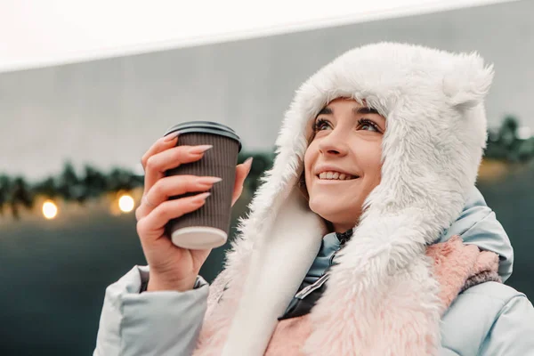 暖かいジャケットとウールの帽子を身に着けていることを祝う若いかなり笑顔の女性は ホットティーコーヒー飲料マルチワインを飲みます 冬の休日 旅行精神リゾート 新年のクリスマスの装飾 ガーランド — ストック写真