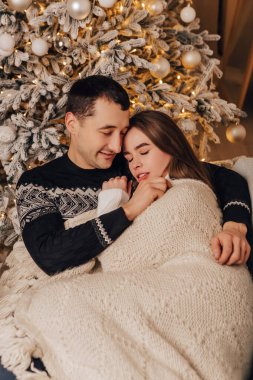 Dikey görüntü sevimli genç romantik çift battaniyenin altında yatıyor, çelenkler ev içinde rahat iç atmosfer yeni yıl ağacı süslemeleri kış akşamını kutlayan Noel partisi 