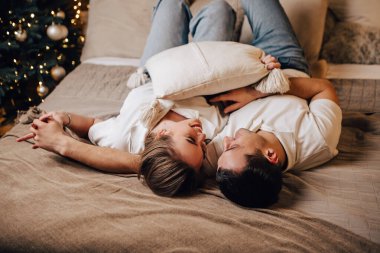 Güzel, genç, romantik bir çift yatağında çelenklerle öpüşüyor. Evlerine sarılıyorlar. Yeni yıl ağacı süslemeleri. 