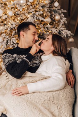 Dikey görüntü sevimli genç romantik çift battaniyenin altında yatıyor, çelenkler ev içinde rahat iç atmosfer yeni yıl ağacı süslemeleri kış akşamını kutlayan Noel partisi 