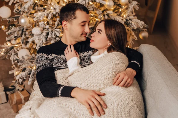 年轻貌美的一对情侣躺在毛毯下 装饰着温馨的室内空气 过年圣诞树装饰节日派对 欢度着冬夜 — 图库照片
