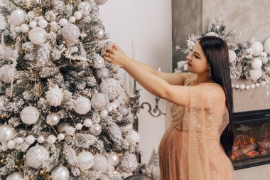 Karnında bebek olan bir kadın Noel Ağacı 'nı süslüyor, yeni yılı kutluyor. Bebek bekleyen hamile bir kadın. Yeni doğmuş bir çocuk bekliyorum.