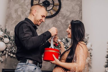 Erkek, yuvarlak göbekli, içinde bebek olan bir kadından hediye alıyor, öpüşüyor, yeni yılı kutluyor, Noel tatilini kutluyor. Bebek bekleyen hamile bir kadın. Yeni doğmuş bir çocuk bekliyorum.