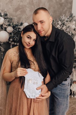 Adamın dikey görüntüsü, göbeği yuvarlak, içinde bebek olan bir kadına sarıldığı, üzerinde erkek giysisi olan, yeni yılı kutlayan bir tişört. Bebek bekleyen hamile bir kadın. Yeni doğmuş bir çocuk bekliyorum.