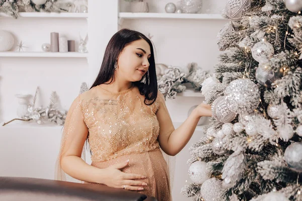 Woman with round belly with baby kid inside decorating Christmas Tree, celebrating New Year holiday. Pregnant lady waiting for infant. Expecting a newborn child