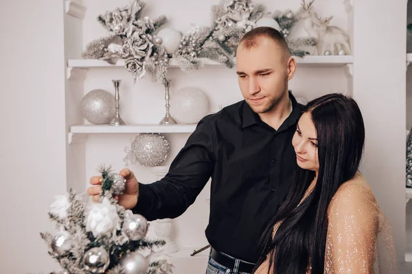Man hug a woman with round belly with baby kid inside decorating Christmas Tree, celebrating New Year holiday. Pregnant lady waiting for infant. Expecting a newborn child