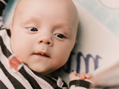 Little boy cute child lying in baby carriage pram buggy having fun smiling laughing, playing making faces grimaces. Toddler playful baby have a walk with mother. Happy childhood. Family concept