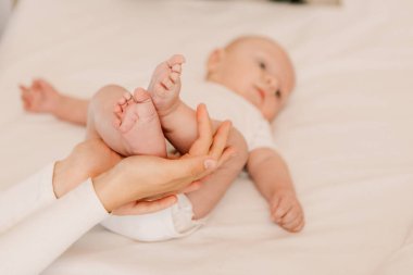 Little funny cute boy, mother hold child legs, baby lying on bed, ready for a diaper change. Playful toddler with bulging eyes having fun, making faces grimaces. Happy childhood, family concept