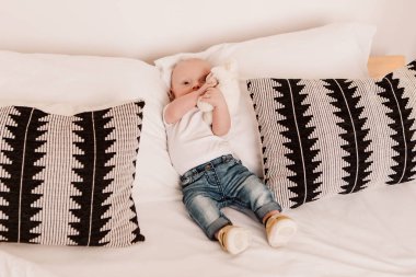 Little boy funny cute child baby lying on bed pillows with fluffy toy. Playful toddler with bulging eyes having fun, making faces grimaces. Happy childhood, family concept