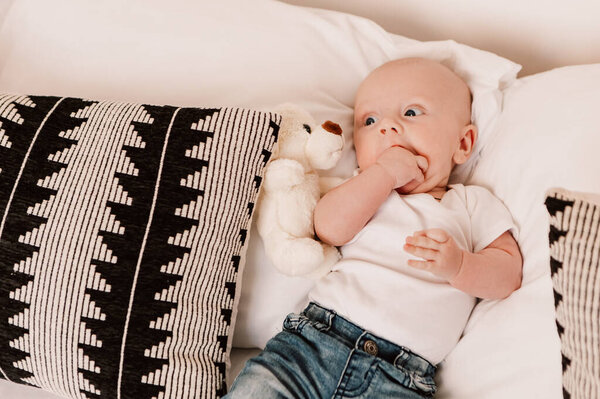 Little boy funny cute child baby lying on bed pillows with fluffy toy. Playful toddler with bulging eyes having fun, making faces grimaces. Happy childhood, family concept