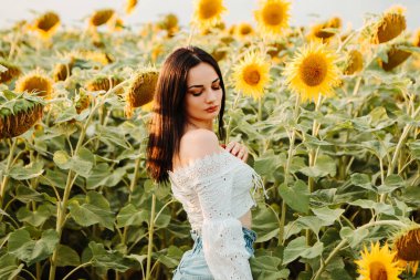 Beautiful young girl model walks through yellow bouquet blooming sunflower field outdoors sunset warm nature background. Woman stopped while travel on weekend copyspace. Summer holiday relax
