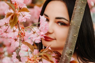 Portrait of beautiful tender woman dressed pink flowery dress posing near sakura cherry blossoms blooming flowers in the garden park in early spring. Hanami celebration, Japanese festival