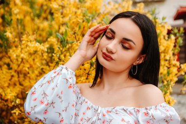 Portrait of beautiful tender woman dressed pink flowery dress posing near yellow forsythia tree blossoms blooming flowers in the garden park in early spring