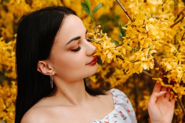 Portrait of beautiful tender woman dressed pink flowery dress posing near yellow forsythia tree blossoms blooming flowers in the garden park in early spring