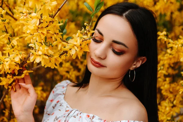 Portrait of beautiful tender woman dressed pink flowery dress posing near yellow forsythia tree blossoms blooming flowers in the garden park in early spring