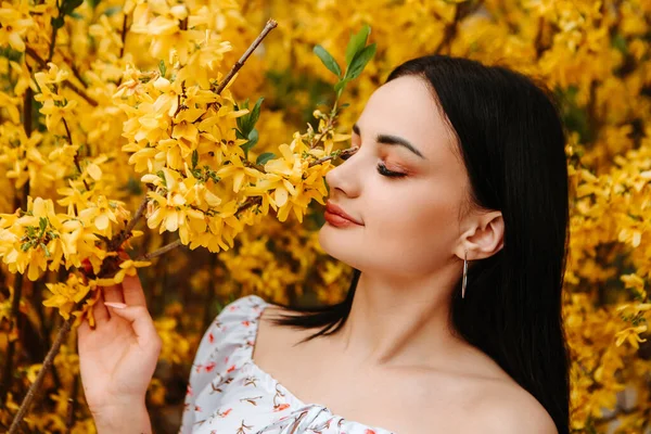 Portrait of beautiful tender woman dressed pink flowery dress posing near yellow forsythia tree blossoms blooming flowers in the garden park in early spring