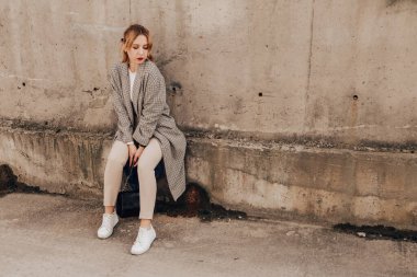 Pretty woman posing near gray wall. Girl dressed casual outfits with red lips. Fashion, make up, hairstyle