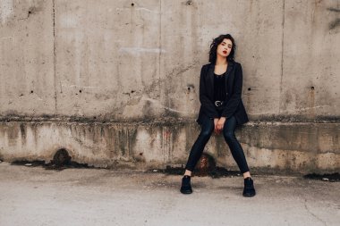 Pretty woman posing near gray wall. Girl dressed casual outfits with red lips. Fashion, make up, hairstyle