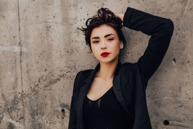 Pretty woman posing near gray wall. Girl dressed casual outfits with red lips. Fashion, make up, hairstyle