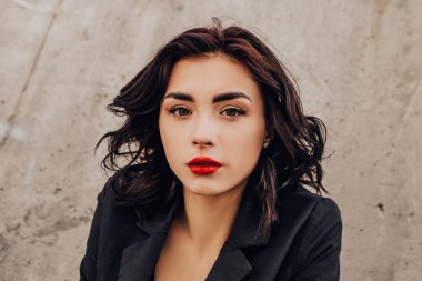 Pretty woman posing near gray wall. Girl dressed casual outfits with red lips. Fashion, make up, hairstyle