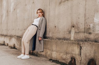 Pretty woman posing near gray wall. Girl dressed casual outfits with red lips. Fashion, make up, hairstyle
