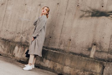 Pretty woman posing near gray wall. Girl dressed casual outfits with red lips. Fashion, make up, hairstyle