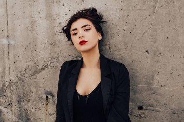 Pretty woman posing near gray wall. Girl dressed casual outfits with red lips. Fashion, make up, hairstyle