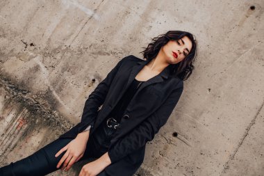 Pretty woman posing near gray wall. Girl dressed casual outfits with red lips. Fashion, make up, hairstyle