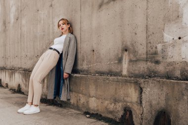 Pretty woman posing near gray wall. Girl dressed casual outfits with red lips. Fashion, make up, hairstyle