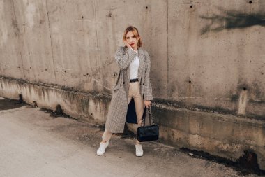 Pretty woman posing near gray wall. Girl dressed casual outfits with red lips. Fashion, make up, hairstyle