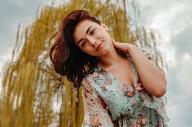 Portrait of charming pretty woman dressed flowery dress posing near willow salix alba tree blossoms blooming in the park in early spring nature. Fashion, girl model with black hair