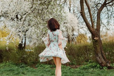 Portrait of charming pretty woman dressed flowery dress spinning around having fun laughing smiling near apple cherry tree blossoms blooming flowers in the garden park in early spring nature