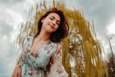 Portrait of charming pretty woman dressed flowery dress posing near willow salix alba tree blossoms blooming in the park in early spring nature. Fashion, girl model with black hair
