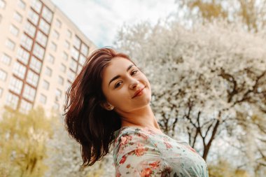 Portrait of charming pretty woman dressed flowery dress posing near apple cherry tree blossoms blooming flowers in the garden park in early spring nature. Fashion, girl model with black hair