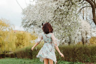 Portrait of charming pretty woman dressed flowery dress spinning around having fun laughing smiling near apple cherry tree blossoms blooming flowers in the garden park in early spring nature