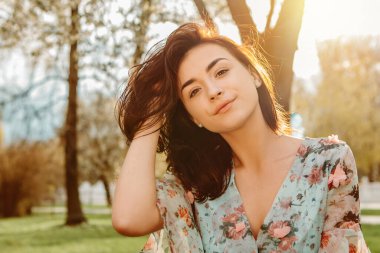 Portrait of charming pretty woman dressed flowery dress sitting on bench near apple cherry tree blossoms blooming flowers in the garden park in early spring nature. Fashion, holiday