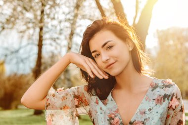 Portrait of charming pretty woman dressed flowery dress sitting on bench near apple cherry tree blossoms blooming flowers in the garden park in early spring nature. Fashion, holiday