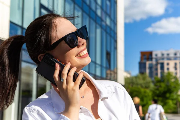Portrait of smiling caucasian woman with white teeth talking on phone, having pleasant conversation, hold mobile device. Perfect healthy smile with veneer. Dental care.