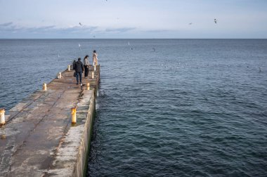 Odessa, Ukrayna 19.02.2023. İnsanlar Ukrayna 'nın Odessa kentindeki Lanzheron plajında bulutlu bir kış günü deniz kenarında yürür.