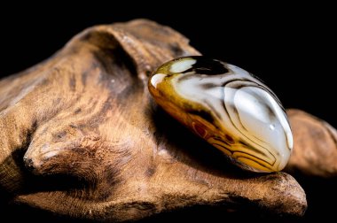 Parlak renkli şeritleri olan parlak, pürüzlü ahşap bir yüzey üzerinde duran parlak bir akik taşının yakın plan fotoğrafı.